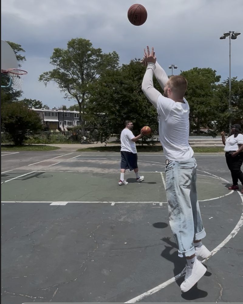 Caleb Johnston taking a jump shot, with the ball and hoop visible, on an outdoor basketball court.